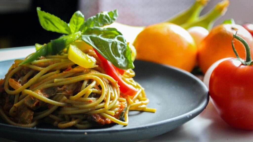 Pasta With Vegetable Dish on Gray Plate Beside Tomato Fruit on White Table