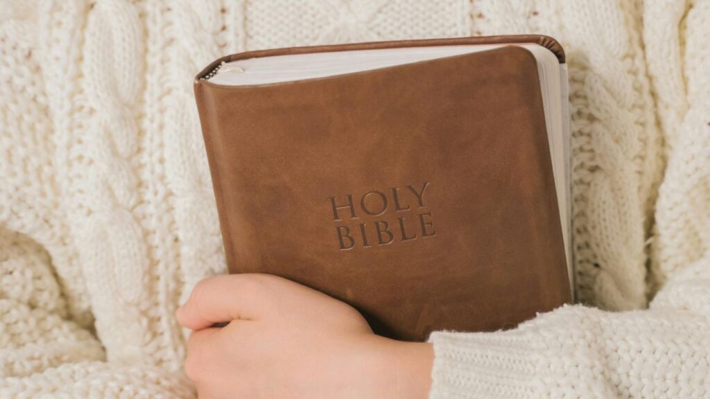 Person in White Sweater Holding Brown Leather Book