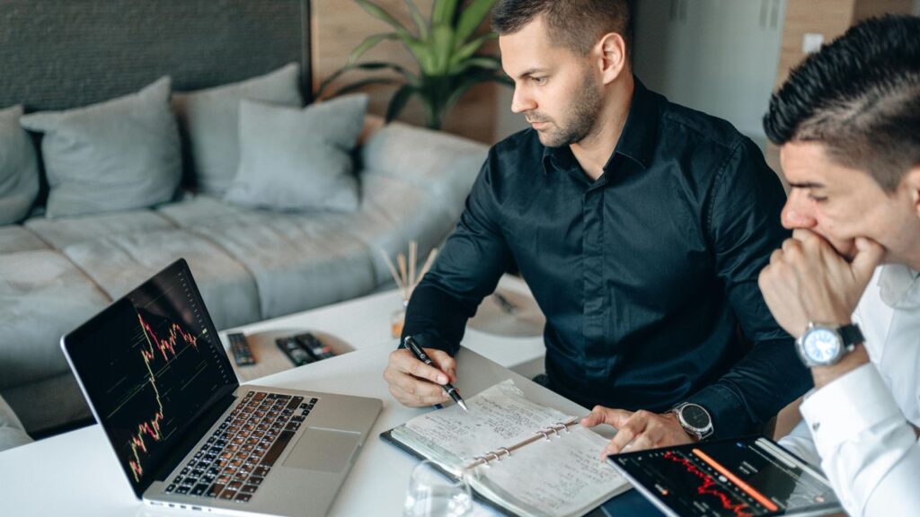 Men Looking at the Laptop Screen While Taking Notes