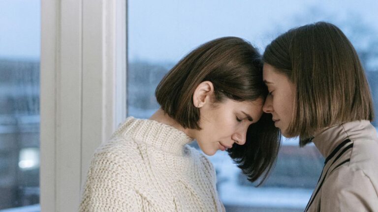 Women Comforting Each Other Near the Glass Window