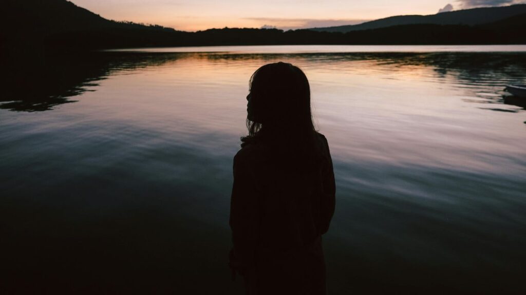 Silhouette Of Woman Standing Near Body Of Water