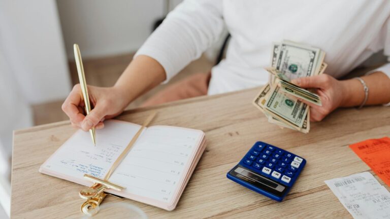 Person Writing on a Notebook while Holding Money