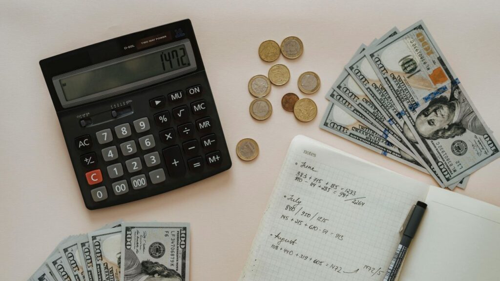 Black Calculator beside Coins and Notebook