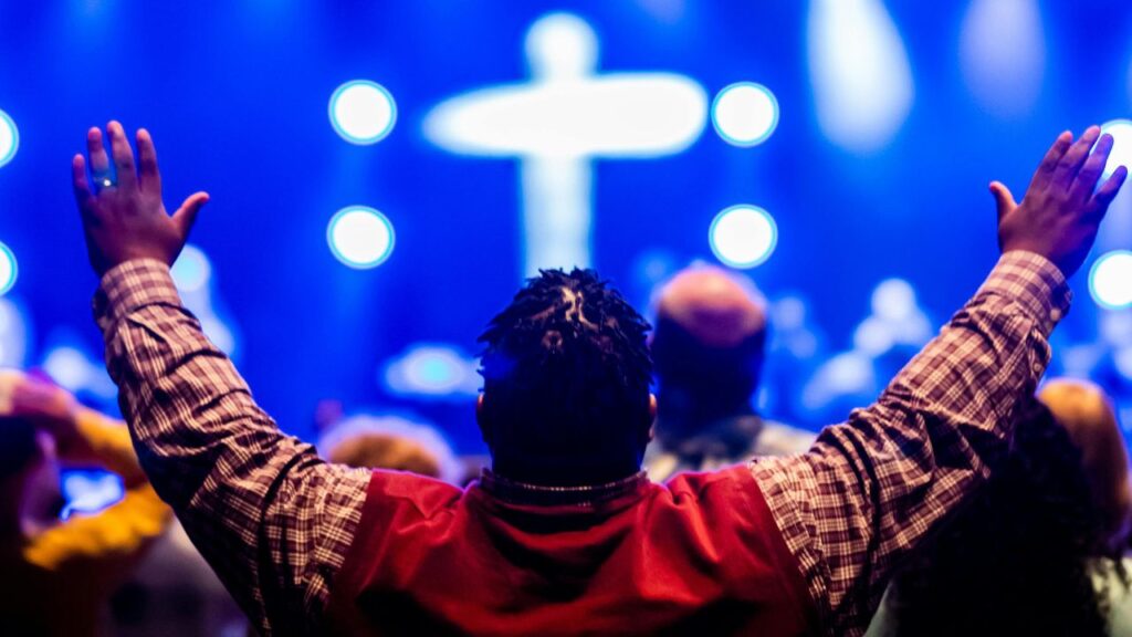 Photo of a Man Raising his Hands towards a Stage with a Cross