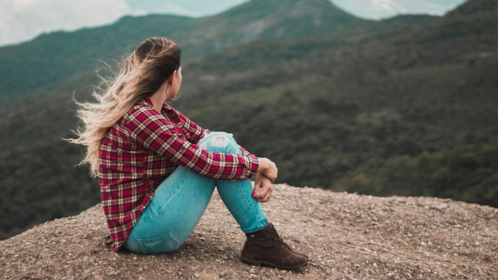Side View Photo of Woman Sitting on Ground Overlooking a Hill