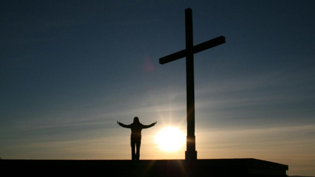 Silhouette of Person Standing Beside Cross during Sunset