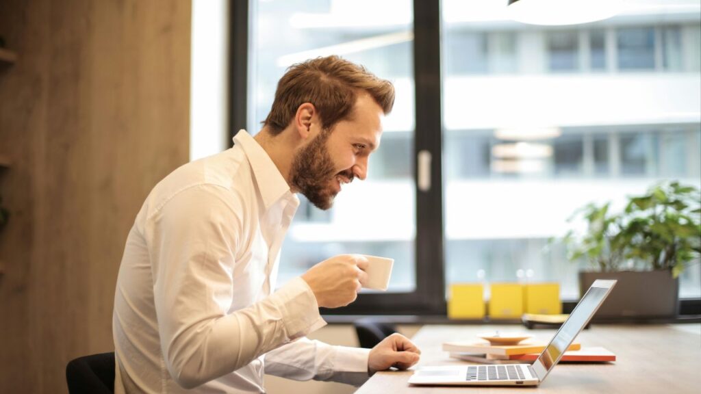 Man Holding Teacup Infront of Laptop on Top of Table Inside the Room