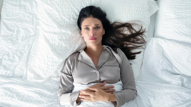 Depressed young woman lying in bed on back and thinking feeling distressed and lonely sad lady