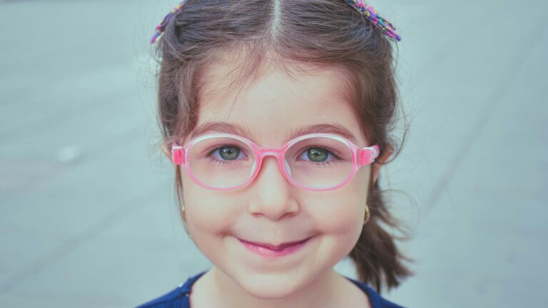 girl in blue and white shirt wearing pink framed eyeglasses