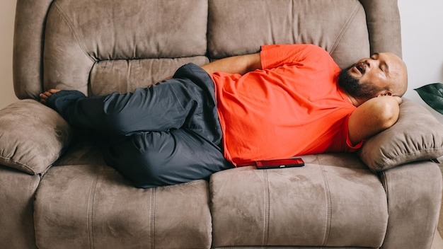 Fat and bald man laying on the couch taking a nap