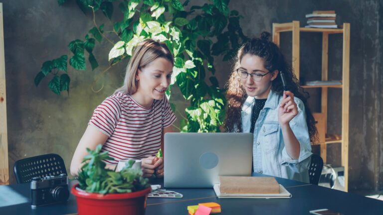 Two women collaborate at a laptop together.