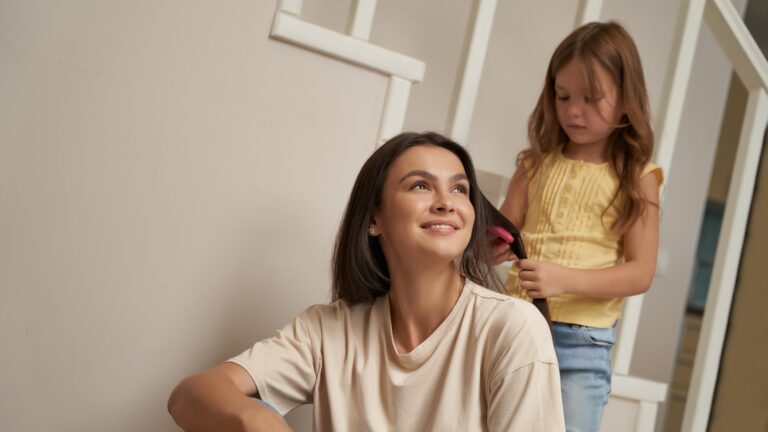 Cute little girl combing long hair of her beautiful smiling mother mom and daughter spending time