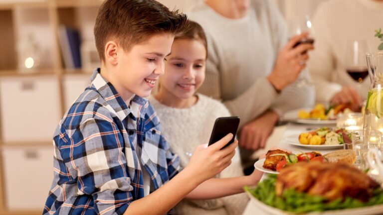 boy with sister using smartphone at family dinner