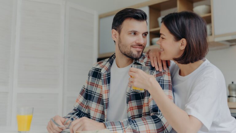 Lovely couple look at each other with love, woman holds glass of juice