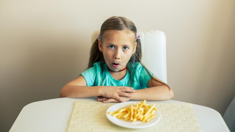 Closeup of a little girl eating french fries at the kitchen