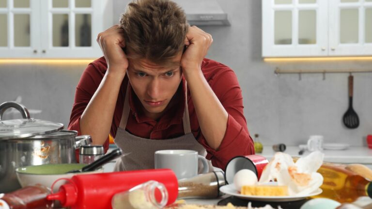 Upset man in messy kitchen Many dirty dishware utensils and food leftovers on table