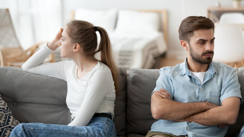 Stubborn couple sit on couch back to back avoid talking after fight offended man and woman separated on sofa ignoring one another husband and wife not looking in eyes Family conflict concept