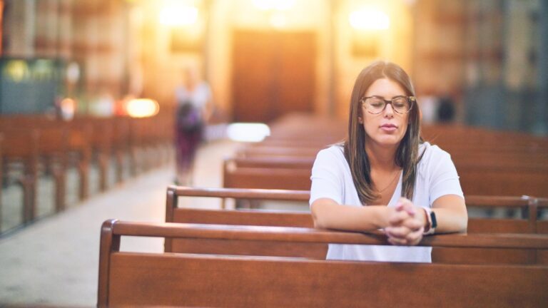 Young beautiful woman praying on her knees in a bench at church