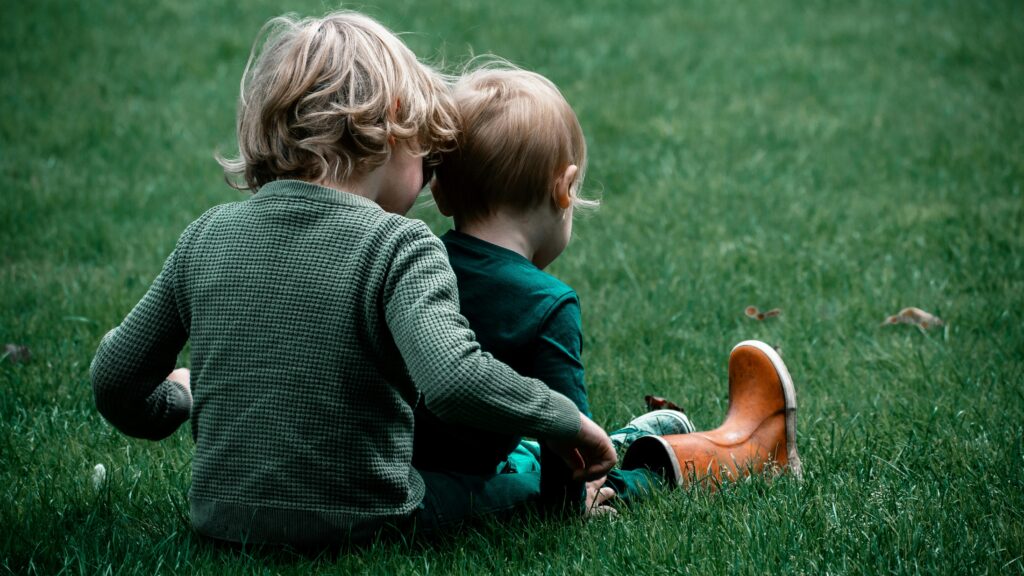 Two children sitting on the grass playing with each other