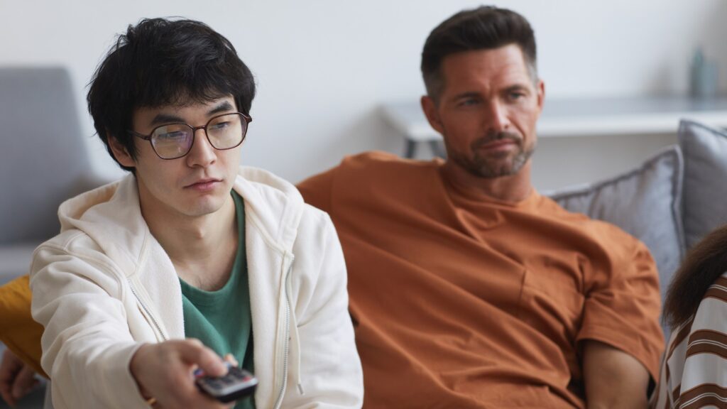 Portrait of young Asian man holding TV remote while watching movies with friends and family at home