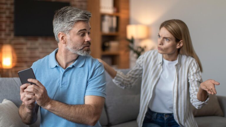 Sad angry middle aged caucasian woman yelling at husband gesticulates man suffers from gadget addiction
