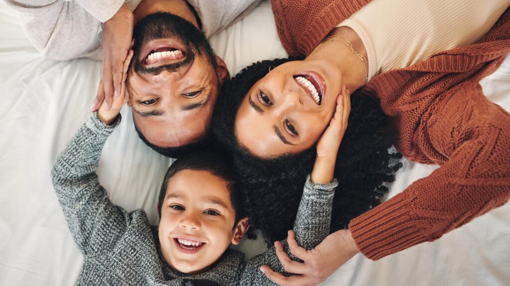 Family laughing and top view portrait on bed in bedroom bonding and care in home Love smile and happy mother comic father and funny boy child playing having fun and enjoying joke time together