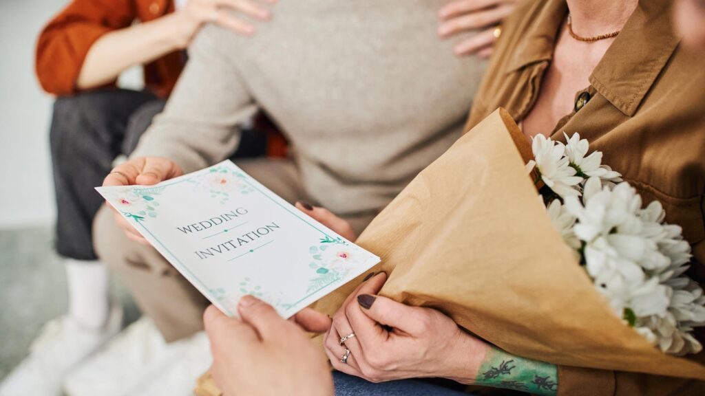 selective focus of wedding invitation near young gay couple and parents sitting at home