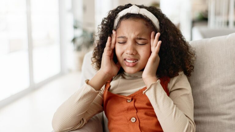 Young girl headache and sofa with stress in anxiety pain or distress for noise at home Little female person child or kid alone with migraine on living room or lounge couch in fatigue or burnout