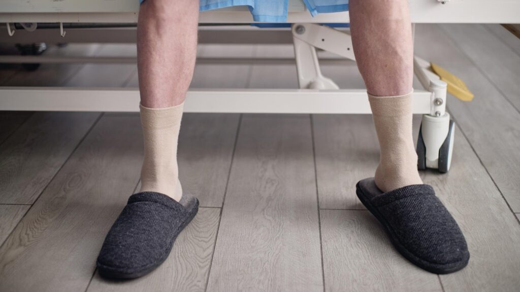 Senior man wearing compression socks sitting on hospital bed resting