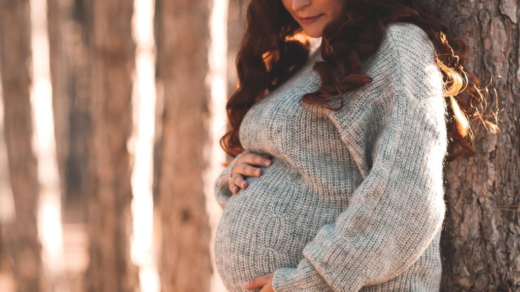Pregnant woman 30-35 year old wearing warm knitted sweater posing outdoors Motherhood