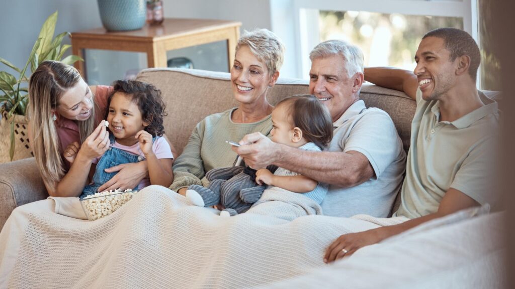 Family children and watching tv grandparents parents and kids together on a sofa in the living room of their home Movie television and film with a man woman and grandkids bonding over a video