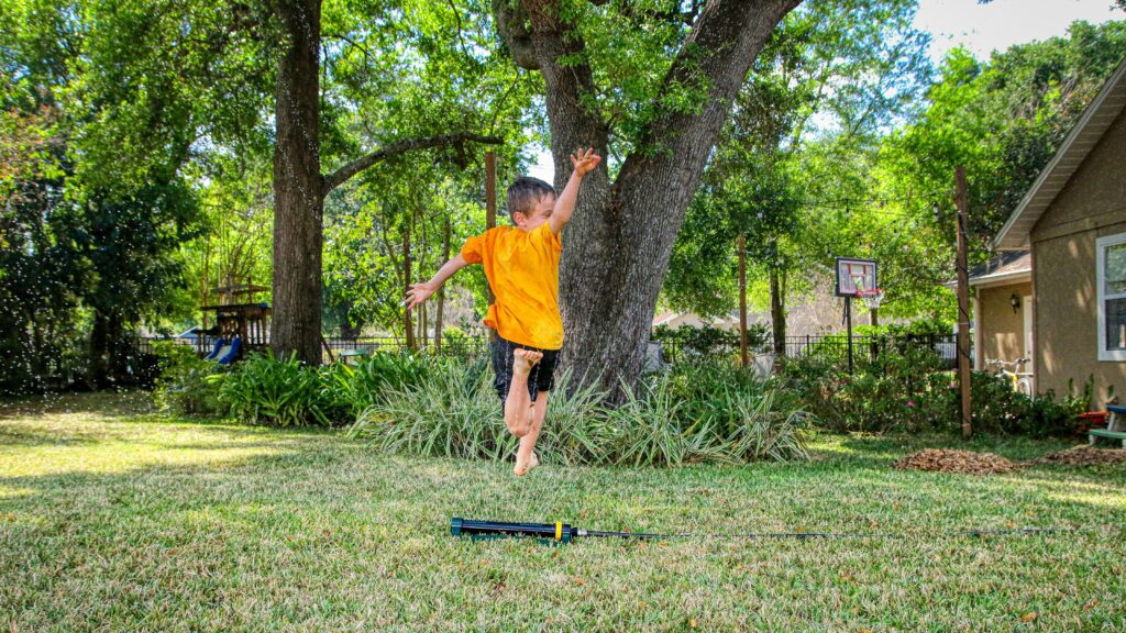 man in orange t-shirt and blue denim shorts standing on green grass field during daytime