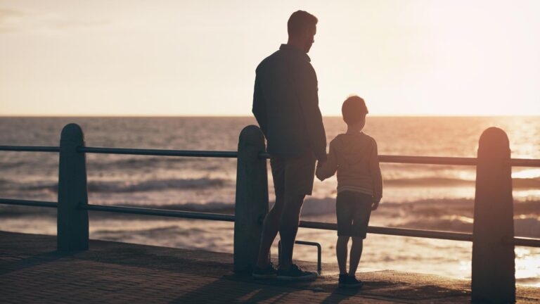 Silhouette sunset and a father holding hands with his son on the promenade at the beach while walking together View family or kids and a man bonding with his young male child outdoor in nature