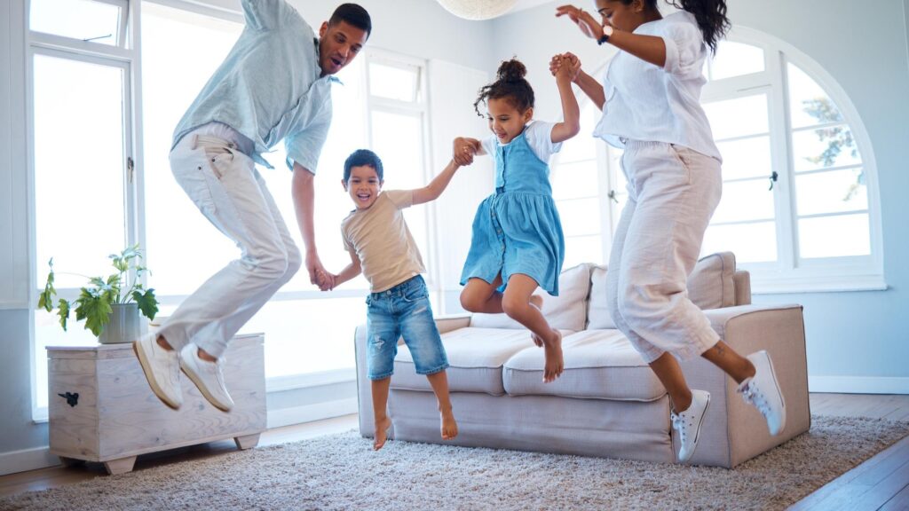 Happy family jumping and playing with energetic children for bonding weekend or holiday at home Mother father and kids enjoying fun activity in air with parents in living room together at house