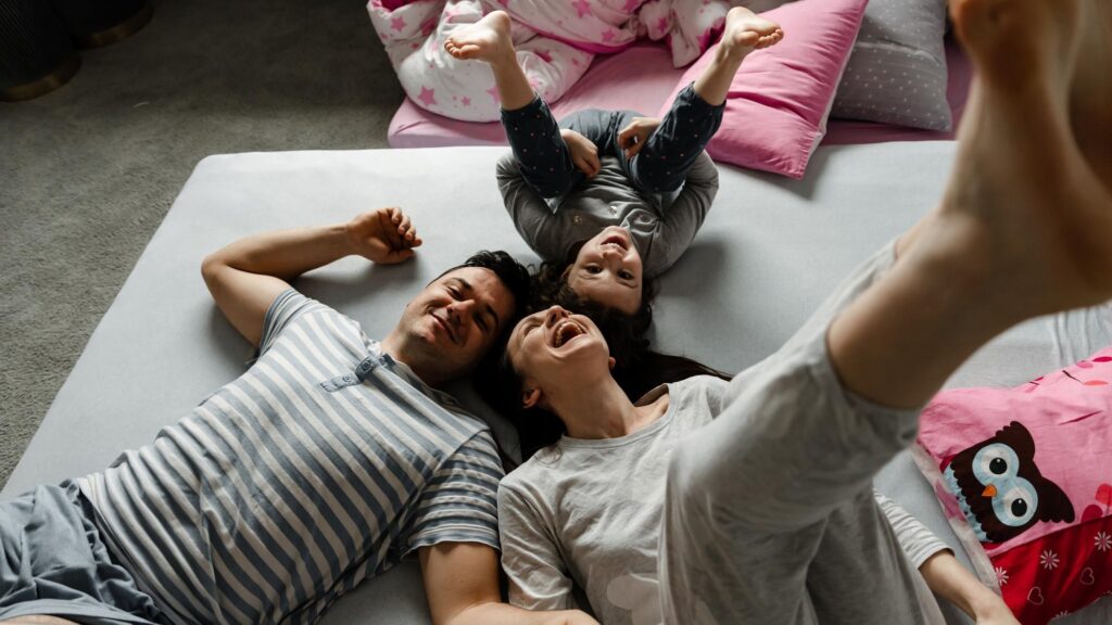 Top view of a cute little girl and her beautiful young parents looking at the camera and smiling, lying on the floor at home,Vvew from above of resting family lying on the floor and looking at camera