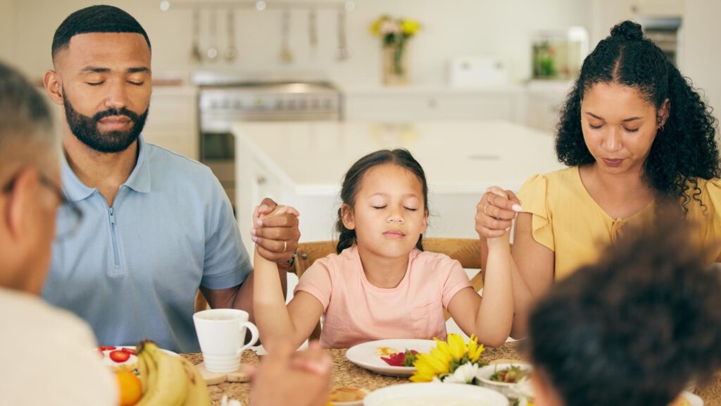 Praying parents and child at table for lunch dinner or breakfast together and holding hands for grace Family religion and mother dad and girl giving thanks gratitude and prayer for food at home