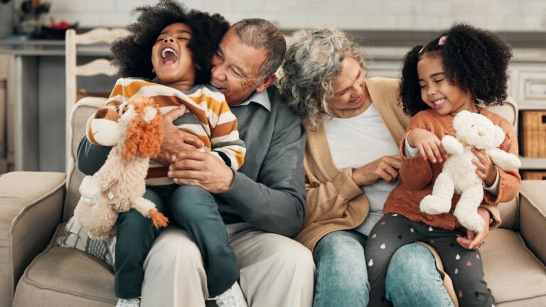 Children laughing or family with grandparents and grandkids bonding in the living room of their home Kids funny or tickle with a senior man woman and grandchildren together on a sofa in the house