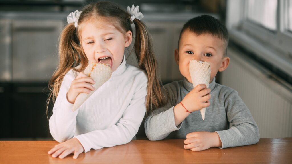 kids boy and girl eating ice cream cone in the kitchen is a lot of fun very sweet