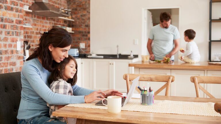 Busy Family Home With Mother Working As Father Prepares Meal