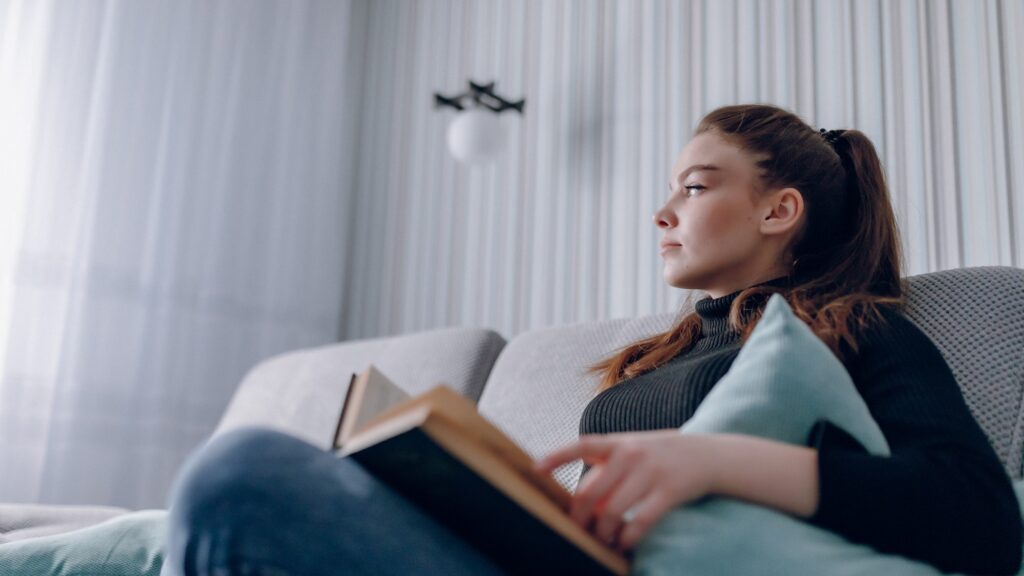 Young attractive girl on the couch reads a paper book. mental development. useful use of time at home. home comfort.
