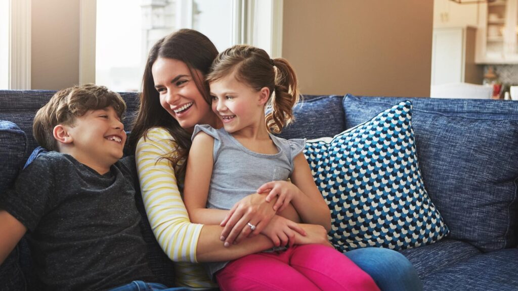 Mom kids and relax on sofa with smile care and together for love and bonding or connection in home Family mother and children in living room with happy embrace and rest on couch in house lounge