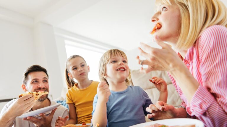 Family of four having meal lunch or dinner eating pizza and having fun at home