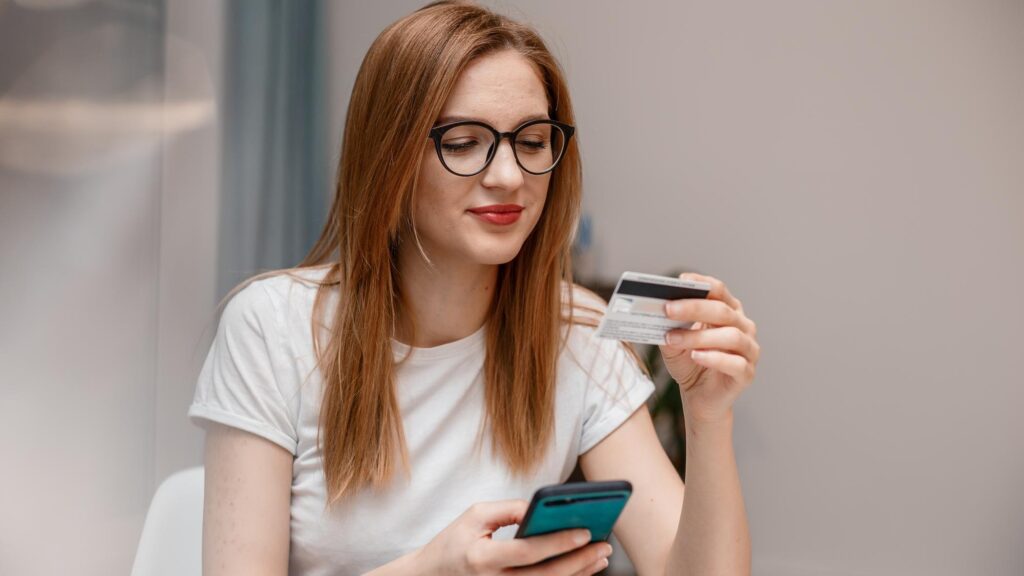 Using smartphone and credit card online shopping Woman using mobile phone app playing game shopping online ordering delivery relax on sofa A Woman shopping Online On Smartphone With A Debit Card