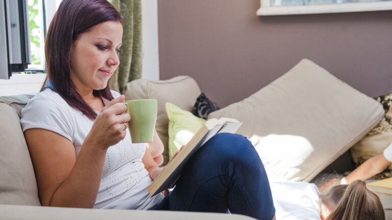 Woman sitting on sofa with cup reading