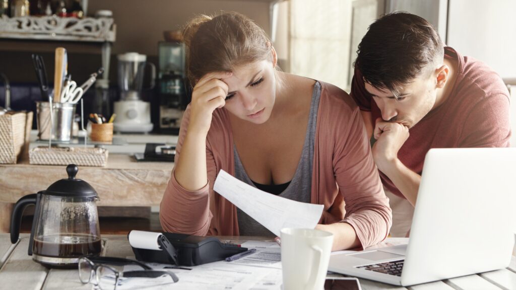 Young married couple facing financial problem during economic crisis. Frustrated woman and unhappy man studying utility bill in kitchen, shocked with amount to be paid for gas and electricity