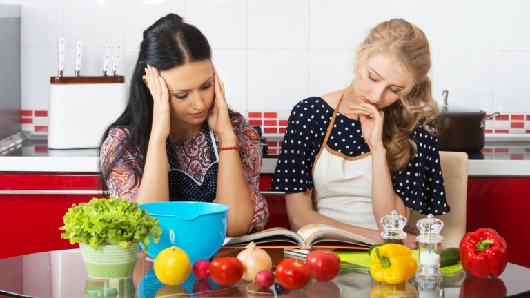Two women in the kitchen cook using cookbook