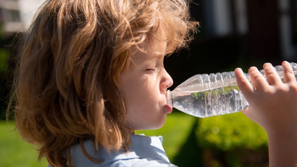 Funny child face close up. Kids drinking water outdoor in park, portrait.