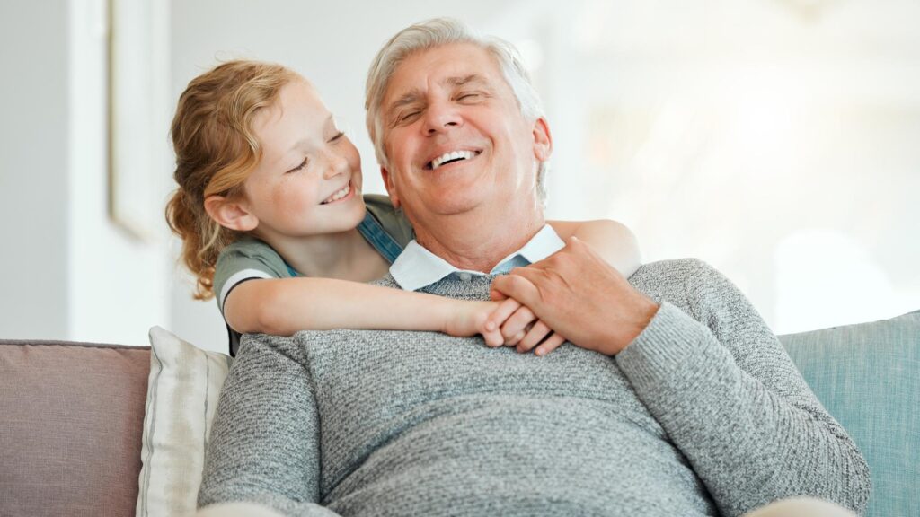 Girl grandfather and relax on sofa with smile for bonding care and embrace on weekend with childhood love Grandpa kid and happy together in family house with hug affection and laughing on couch