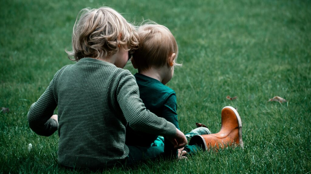 Two children sitting on the grass playing with each other
