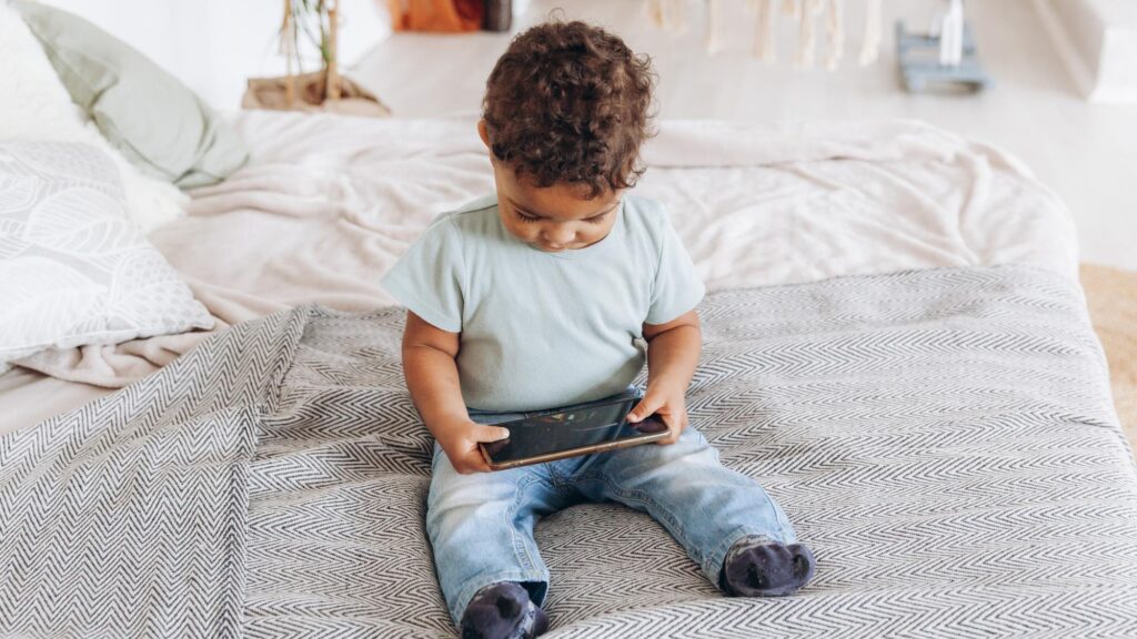Cute little african american boy with smartphone at home on bed happy kid watching cartoons on phone